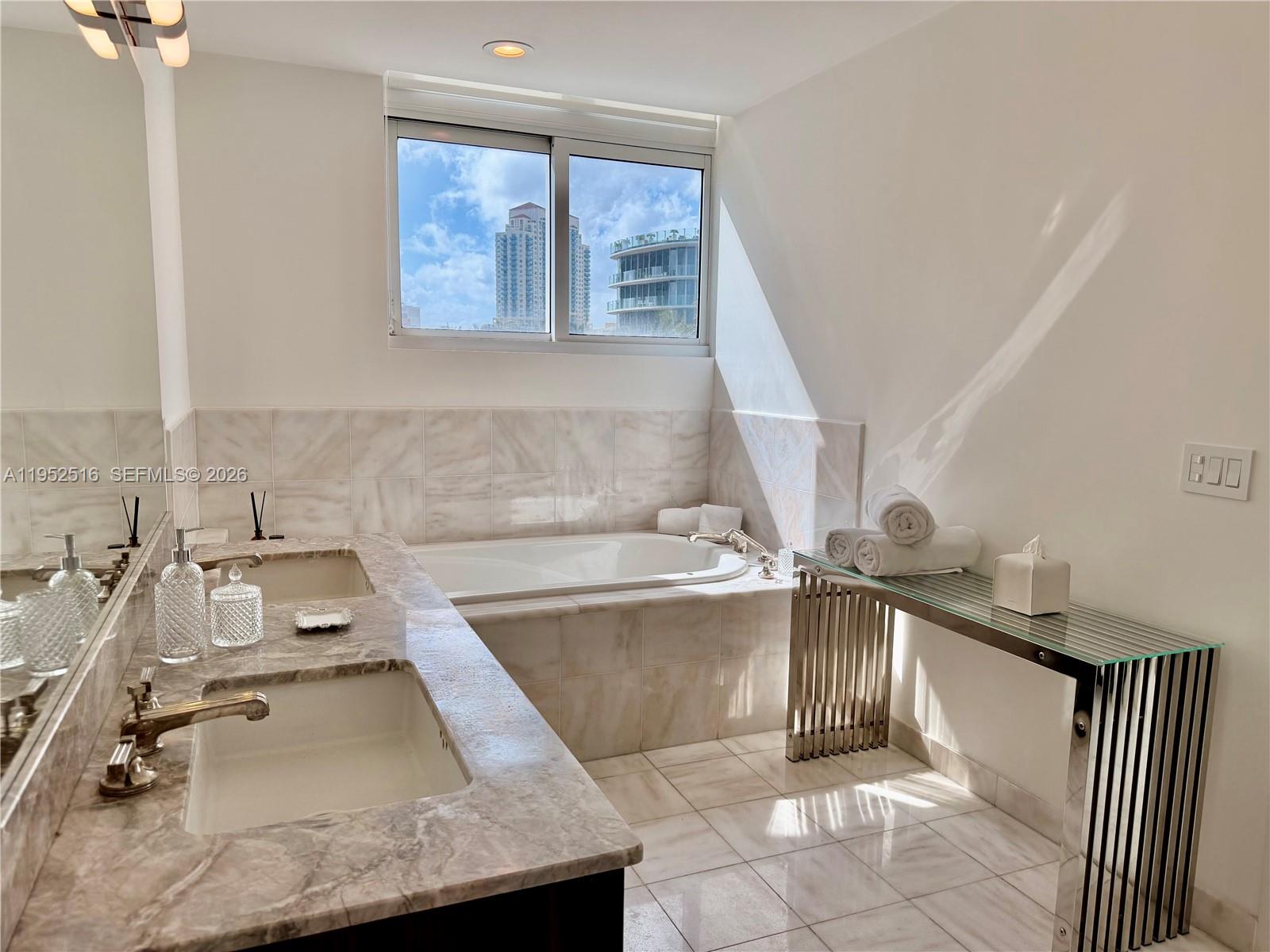 A bathroom features a double vanity, a soaking tub, and a glass-topped console table — 50 S Pointe Dr, Miami Beach FL 33139, MIAMI BEACH, FL