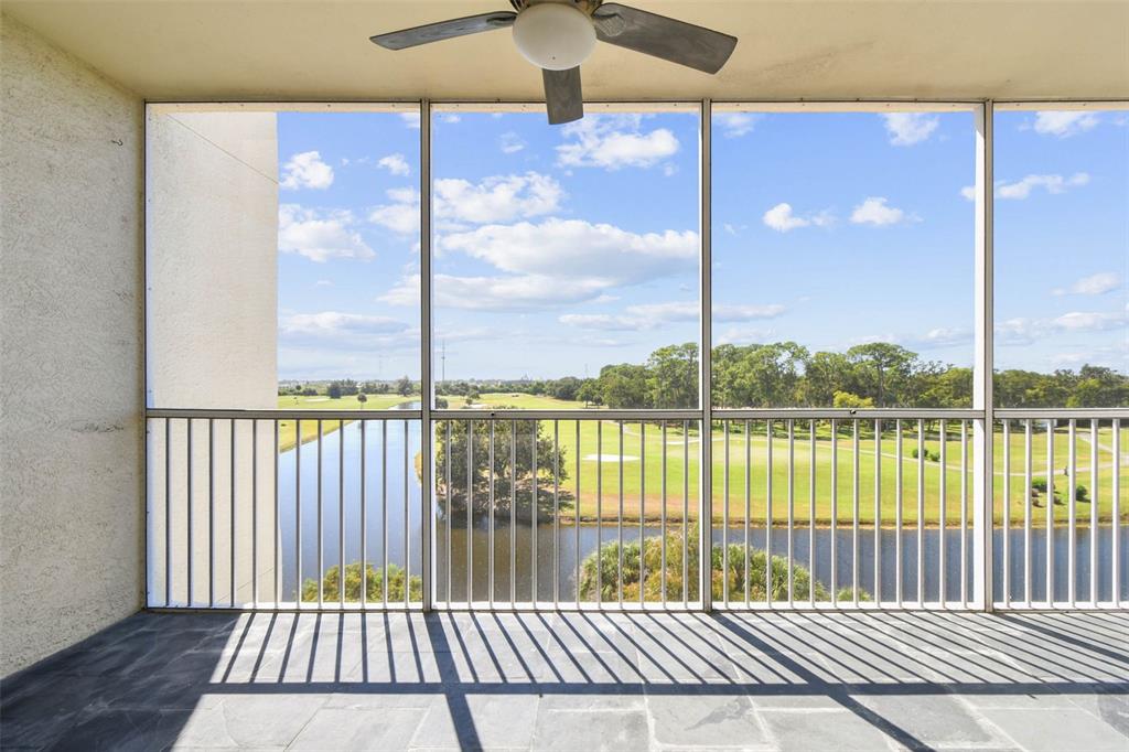A screened-in balcony features a ceiling fan, stone flooring, and a view of a golf course — 1200 COUNTRY CLUB DRIVE UNIT 2405, LARGO, FL