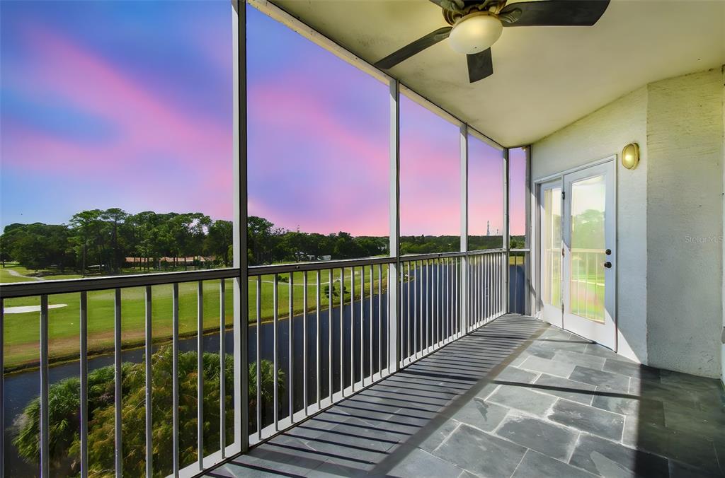 A screened-in balcony with slate tile flooring overlooks a golf course and a pond — 1200 COUNTRY CLUB DRIVE UNIT 2405, LARGO, FL