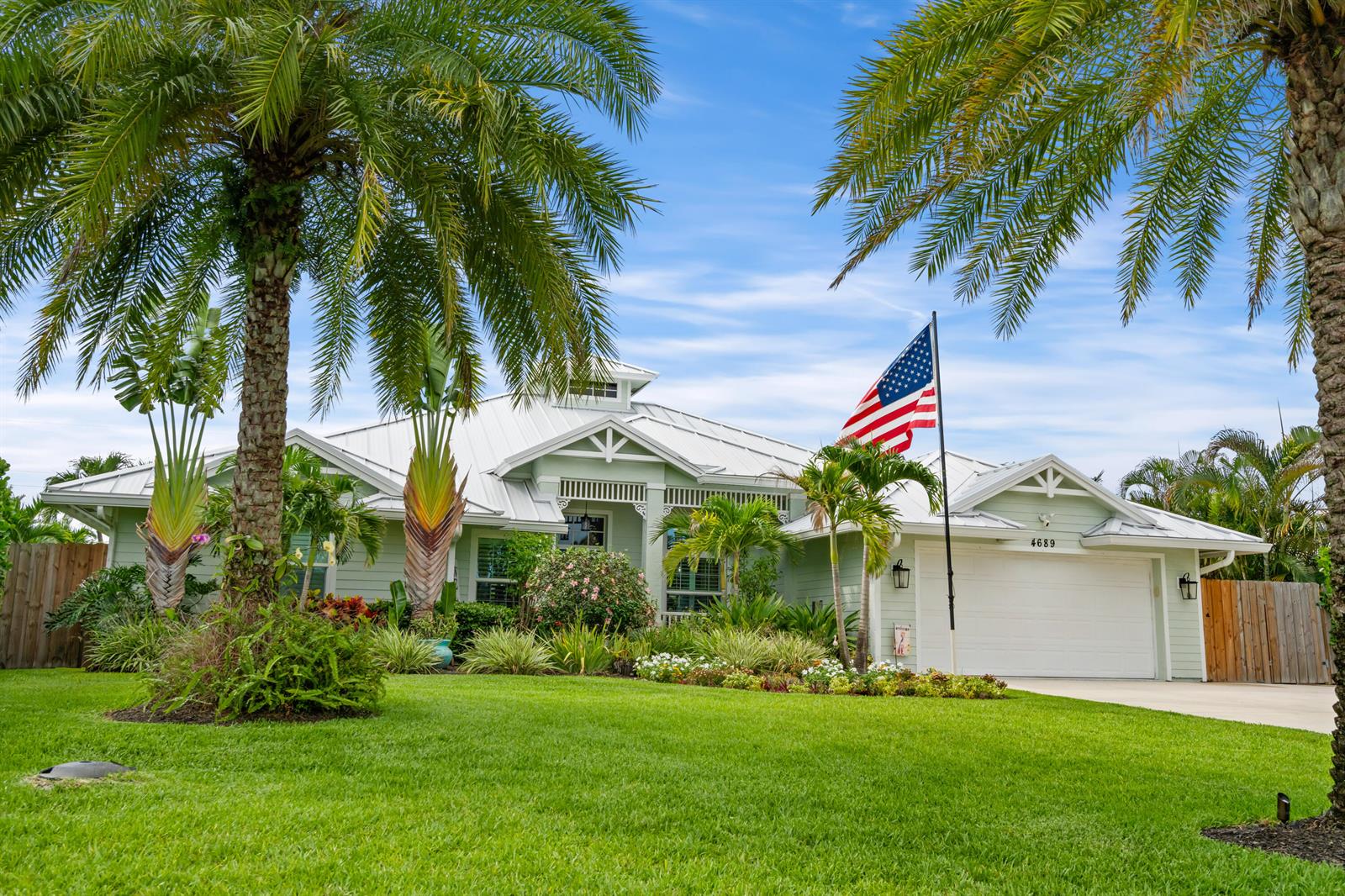 A light green single-story house with a metal roof, palm trees, and an American flag — 4689 SE Glen Ridge Trail, Stuart FL 34997, STUART, FL