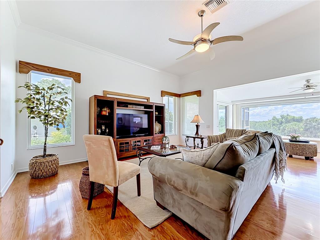 A living room features hardwood floors, a large entertainment center, and a ceiling fan — 6042 TOPSAIL ROAD UNIT 6042, LADY LAKE, FL