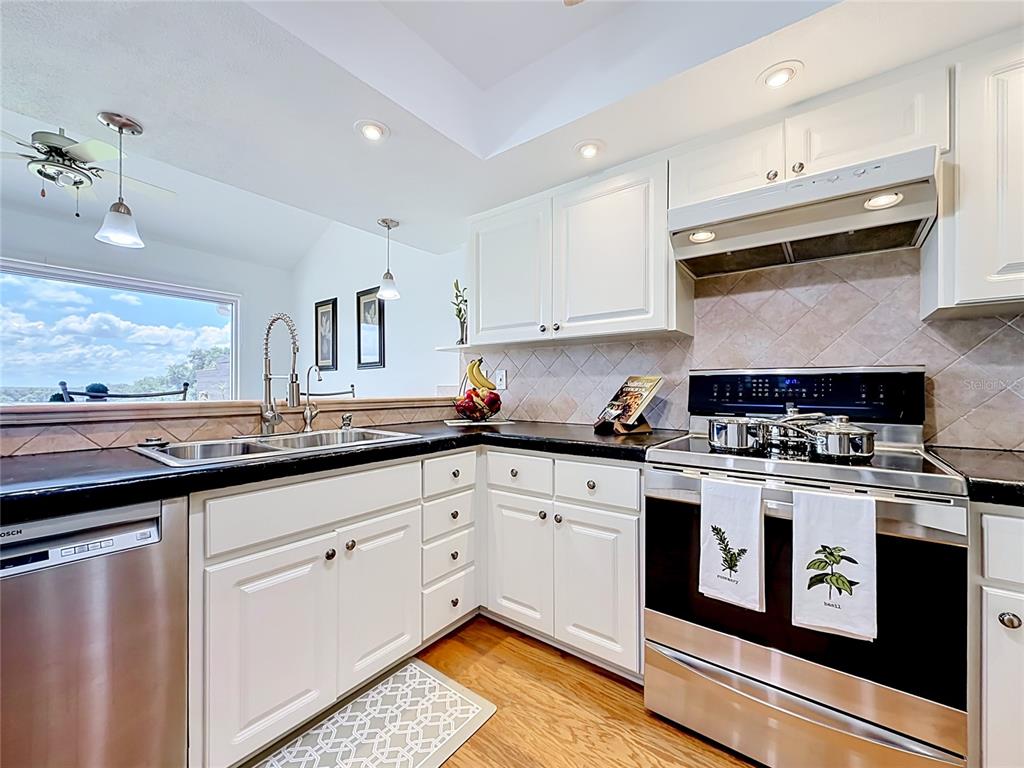 A kitchen features white cabinets, black countertops, stainless steel appliances, and a window view — 6042 TOPSAIL ROAD UNIT 6042, LADY LAKE, FL