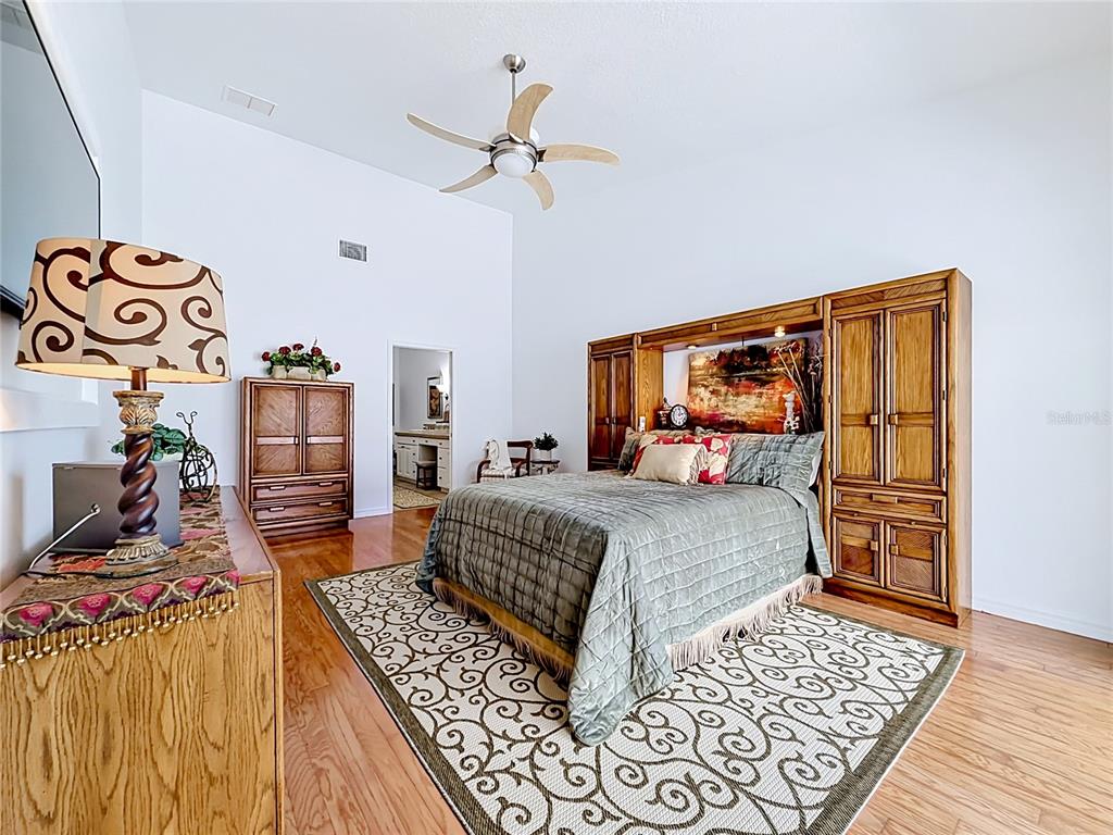 A bedroom features a wooden bed frame, a patterned area rug, and a ceiling fan — 6042 TOPSAIL ROAD UNIT 6042, LADY LAKE, FL