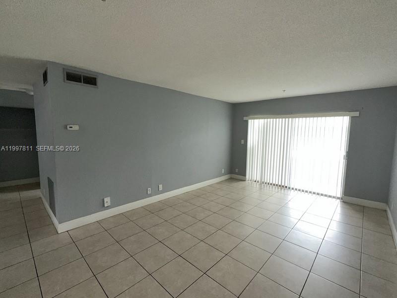 An unfurnished living room features light gray walls, tile flooring, and a large sliding glass door — 4251 NW 5th St # 108, Plantation FL 33317, PLANTATION, FL