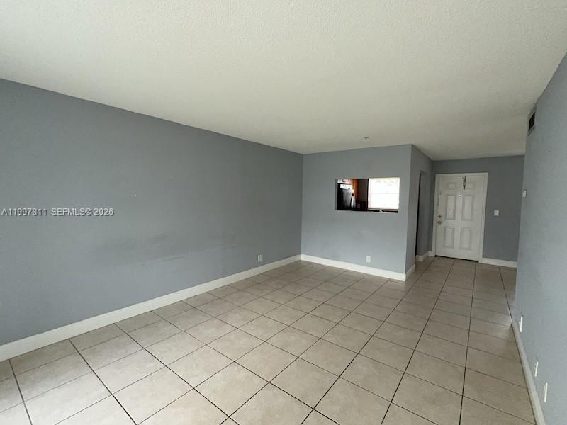 An empty room features light gray walls, tiled flooring, and a pass-through window to the kitchen — 4251 NW 5th St # 108, Plantation FL 33317, PLANTATION, FL