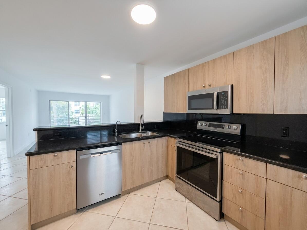 A kitchen with light wood cabinets, black countertops, stainless steel appliances, and tile flooring — 1541 S Ocean Boulevard # 219, Pompano Beach FL 33062, POMPANO BEACH, FL