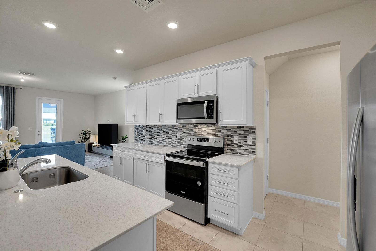 A kitchen features white cabinets, a mosaic tile backsplash, stainless steel appliances, and quartz countertops — 2293 S Appleton Circle, Oakland Park FL 33309, OAKLAND PARK, FL