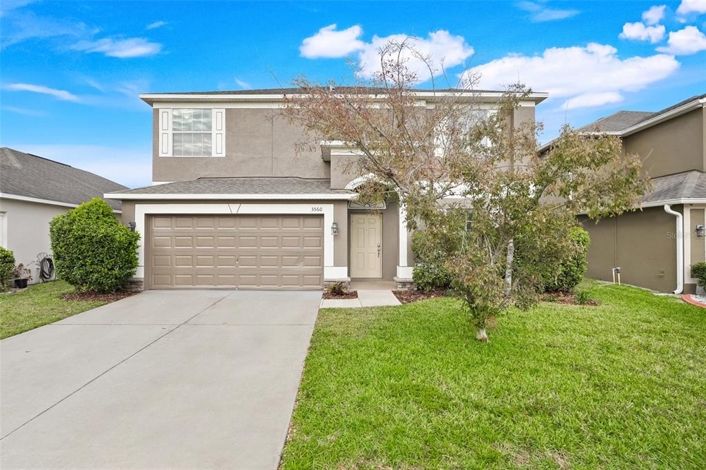 A two-story suburban house features a tan stucco exterior, a two-car garage, and a lawn — 3560 CORTLAND DRIVE, DAVENPORT, FL