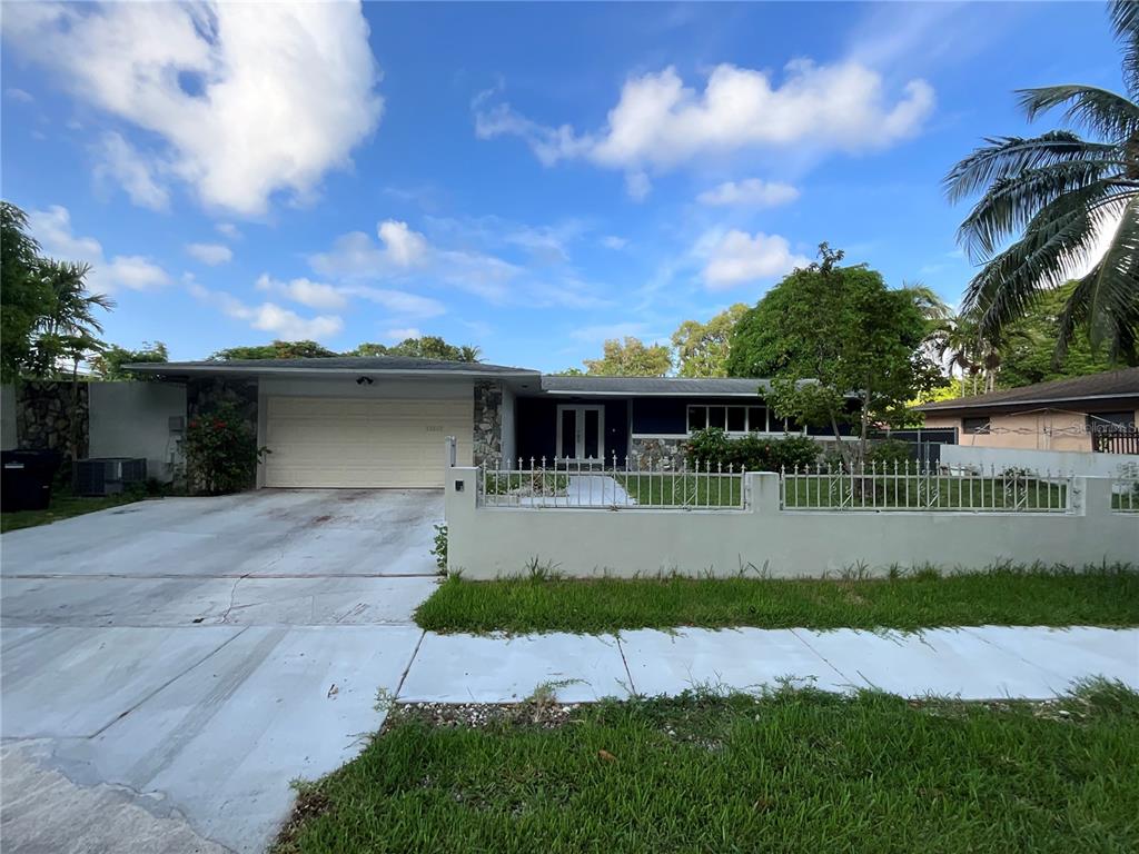 A single-story house with a two-car garage, stone accents, and a white metal fence — 12325 NE 2ND COURT, NORTH MIAMI, FL