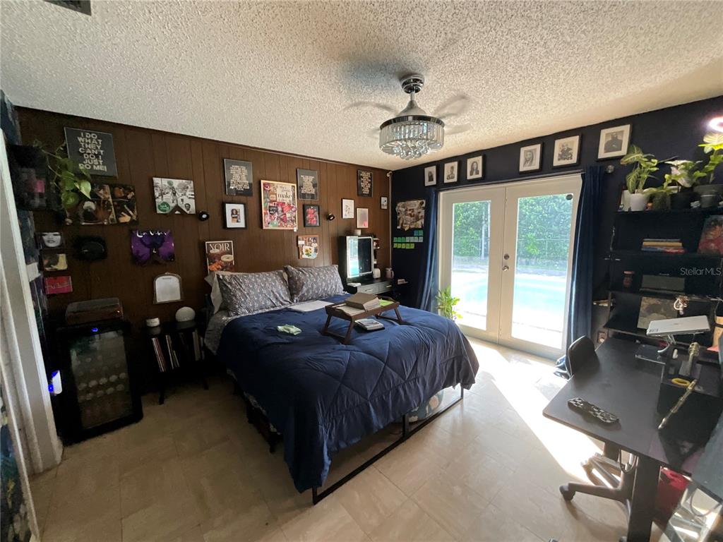 A bedroom features wood-paneled walls, a dark blue bed, a desk, and glass doors to a pool — 12325 NE 2ND COURT, NORTH MIAMI, FL