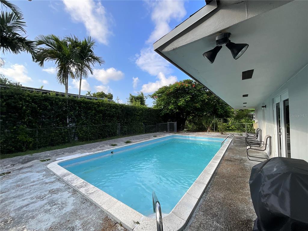 An outdoor rectangular swimming pool sits on a concrete patio next to a house exterior — 12325 NE 2ND COURT, NORTH MIAMI, FL