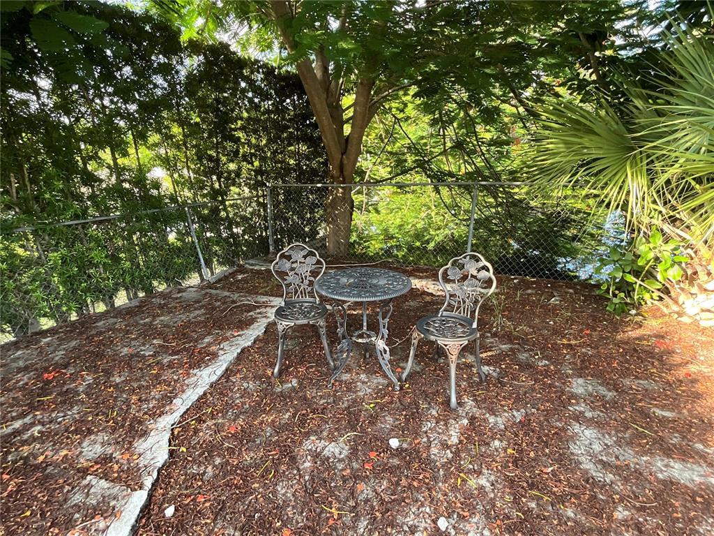 A small metal bistro set sits on a dirt patch beneath a tree near a fence — 12325 NE 2ND COURT, NORTH MIAMI, FL
