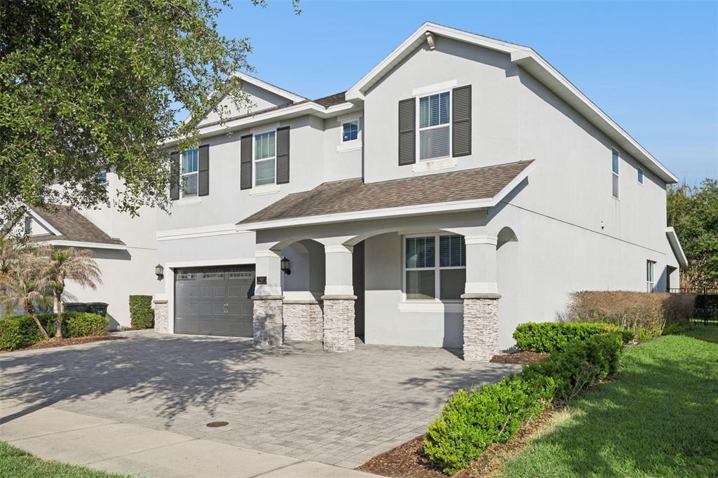 A two-story house with a gray stucco exterior, stone accents, and a paved driveway — 7457 MARKER AVENUE, KISSIMMEE, FL