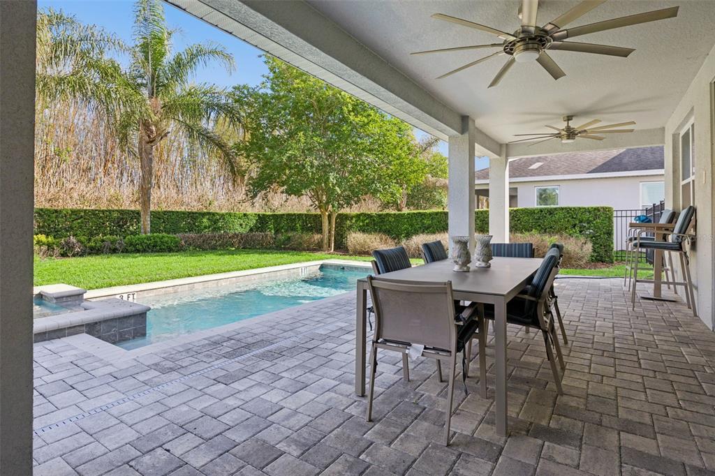 A covered patio features a dining set, ceiling fans, and a pool overlooking a yard — 7457 MARKER AVENUE, KISSIMMEE, FL