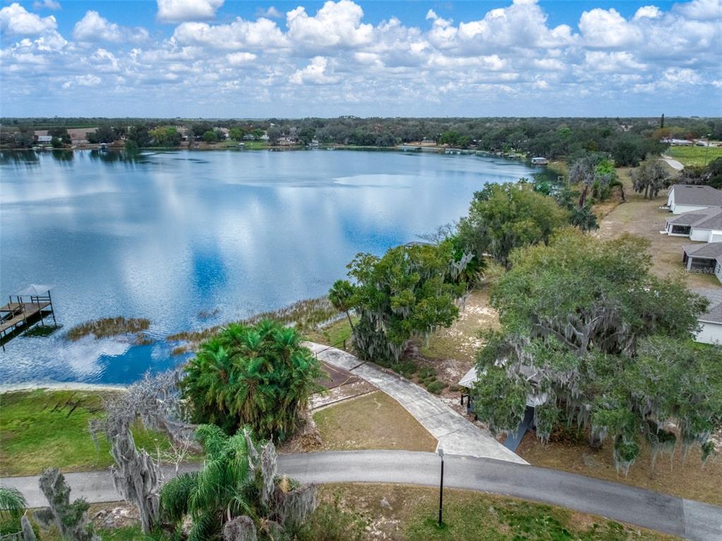 An aerial view shows a lake with a wooden dock, trees, and a paved driveway — 1204 RIDGE DRIVE, AVON PARK, FL