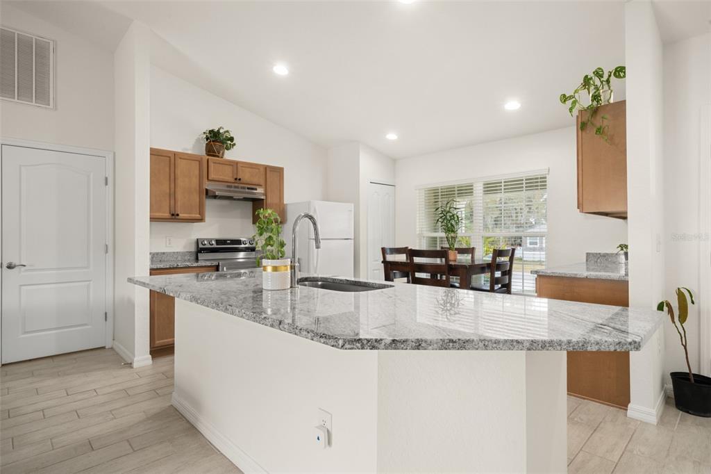 A kitchen with a granite-topped island, wooden cabinets, and a dining area by a window — 1204 RIDGE DRIVE, AVON PARK, FL