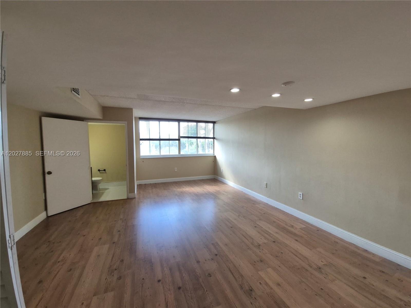 An empty room features wood-look flooring, recessed lighting, and an attached bathroom with a toilet — 6045 NW 186th St # 308, Hialeah FL 33015, HIALEAH, FL