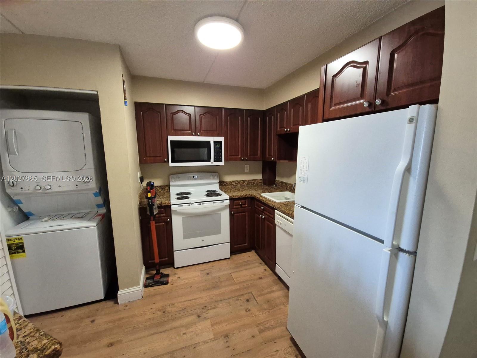 A kitchen features dark wood cabinets, white appliances, granite countertops, and light wood-look flooring — 6045 NW 186th St # 308, Hialeah FL 33015, HIALEAH, FL