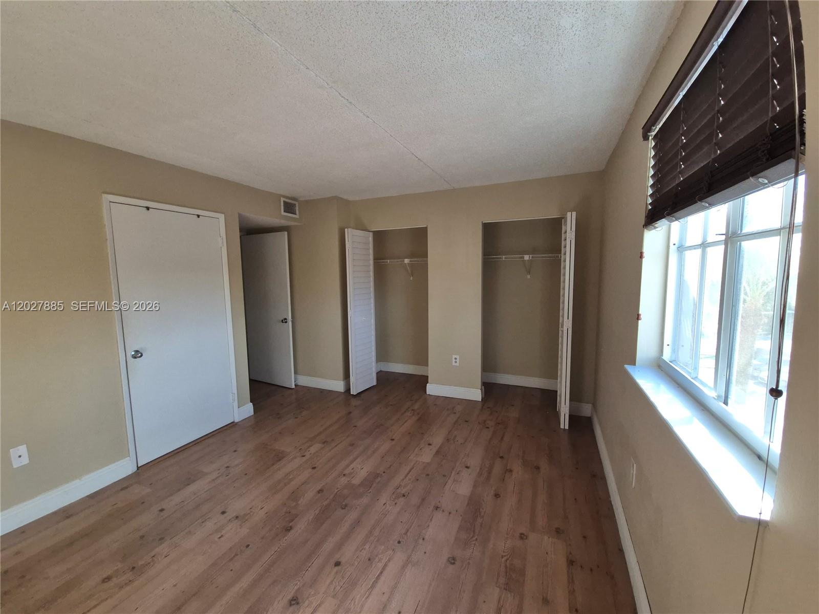 A bedroom with wood-look flooring, two closets, and a window with dark blinds — 6045 NW 186th St # 308, Hialeah FL 33015, HIALEAH, FL