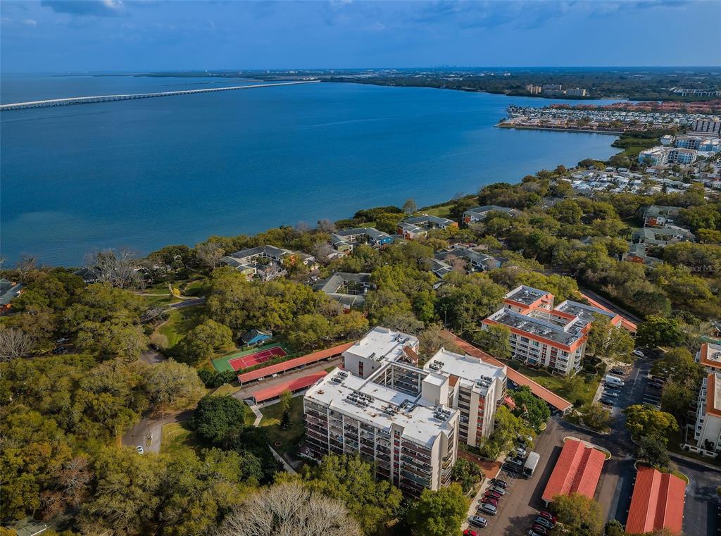 An aerial view shows apartment buildings, a tennis court, and a bridge spanning the water — 2699 SEVILLE BOULEVARD UNIT 105, CLEARWATER, FL