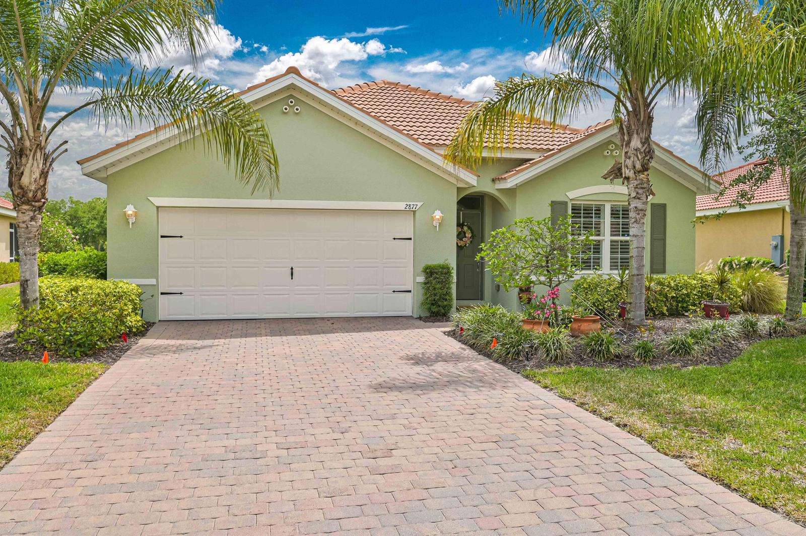 A light green single-story house with a tiled roof, two-car garage, and a paver driveway — 2877 Apple Blossom Drive, FL 33920, FL
