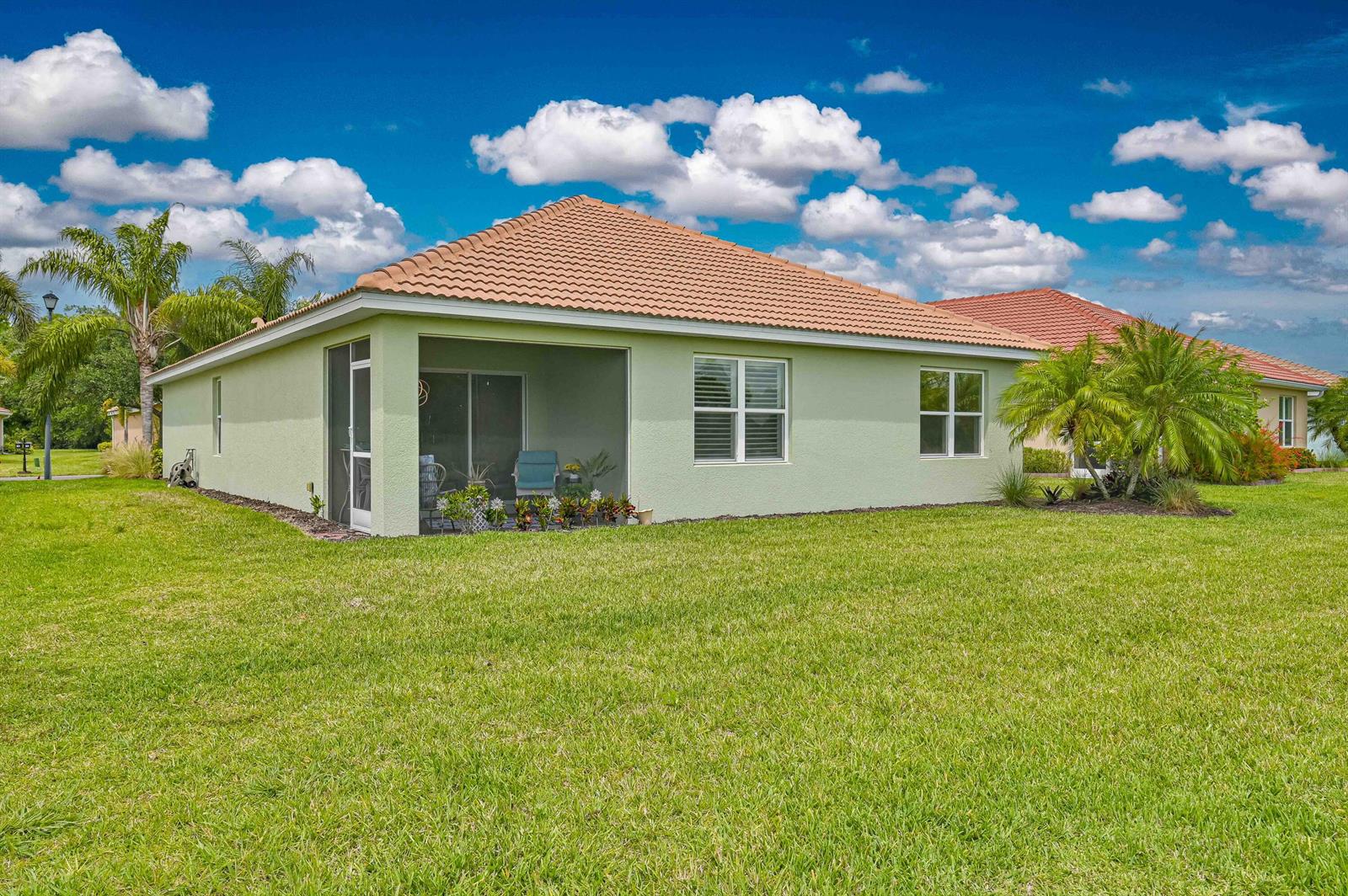 A light green house with a tiled roof and a screened-in patio sits on grass — 2877 Apple Blossom Drive, FL 33920, FL
