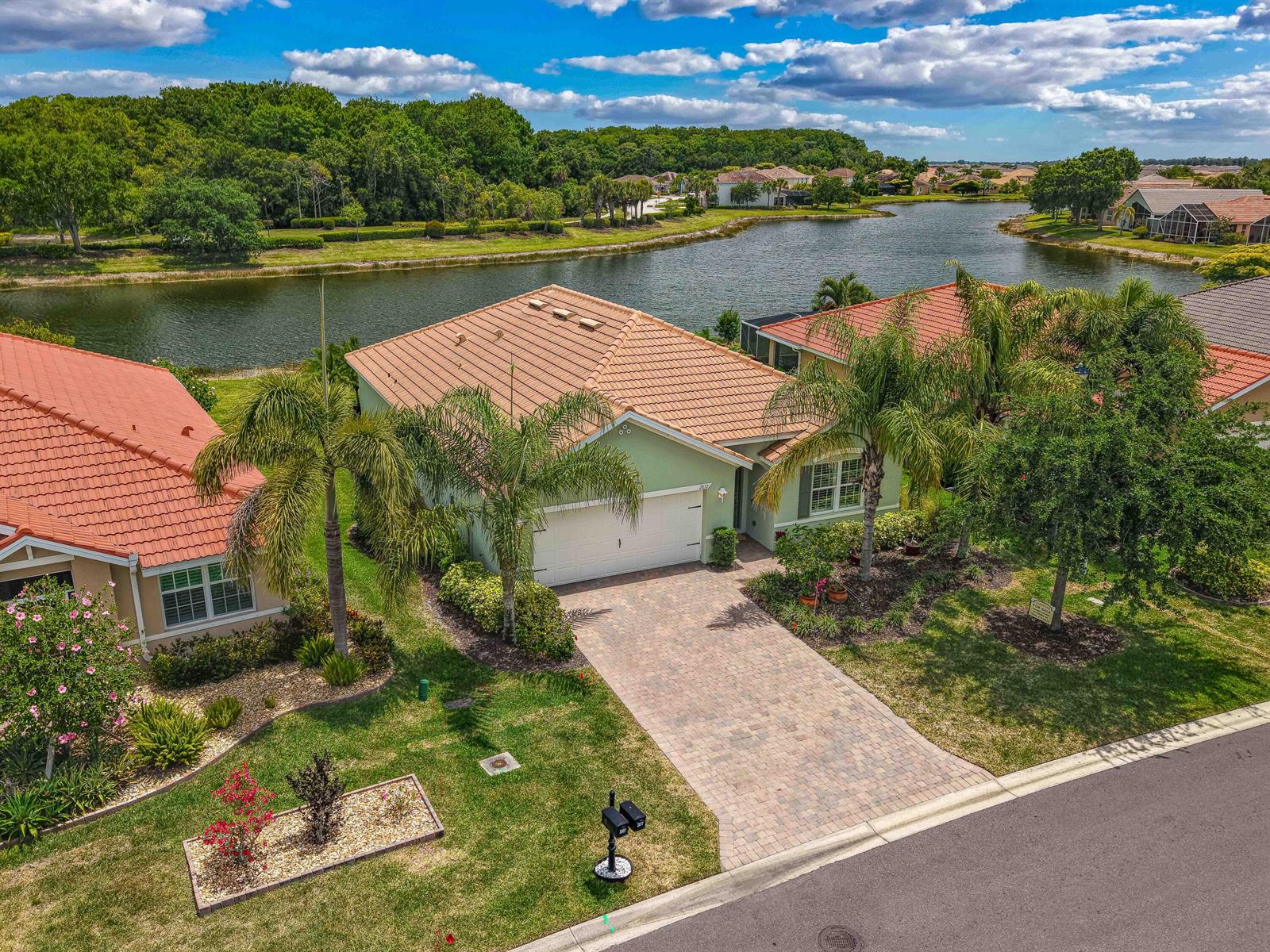 An aerial view shows a light green house with a tiled roof, driveway, and lakefront backyard — 2877 Apple Blossom Drive, FL 33920, FL