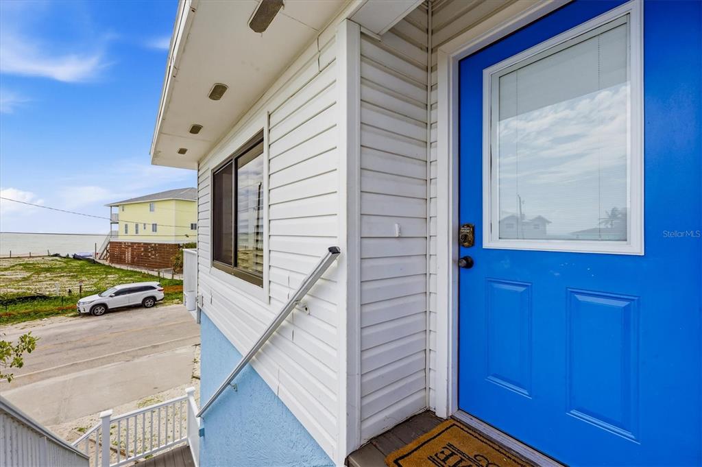 A bright blue door with a window sits beside white horizontal siding on an elevated porch — 1245 SHORE VIEW DRIVE, ENGLEWOOD, FL
