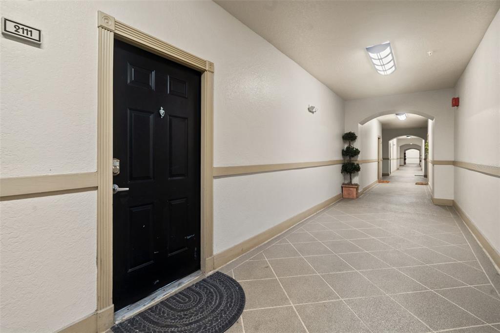 A black apartment door with the number 2111 sits in a long, tiled indoor hallway — 501 KNIGHTS RUN AVENUE UNIT 2111, TAMPA, FL