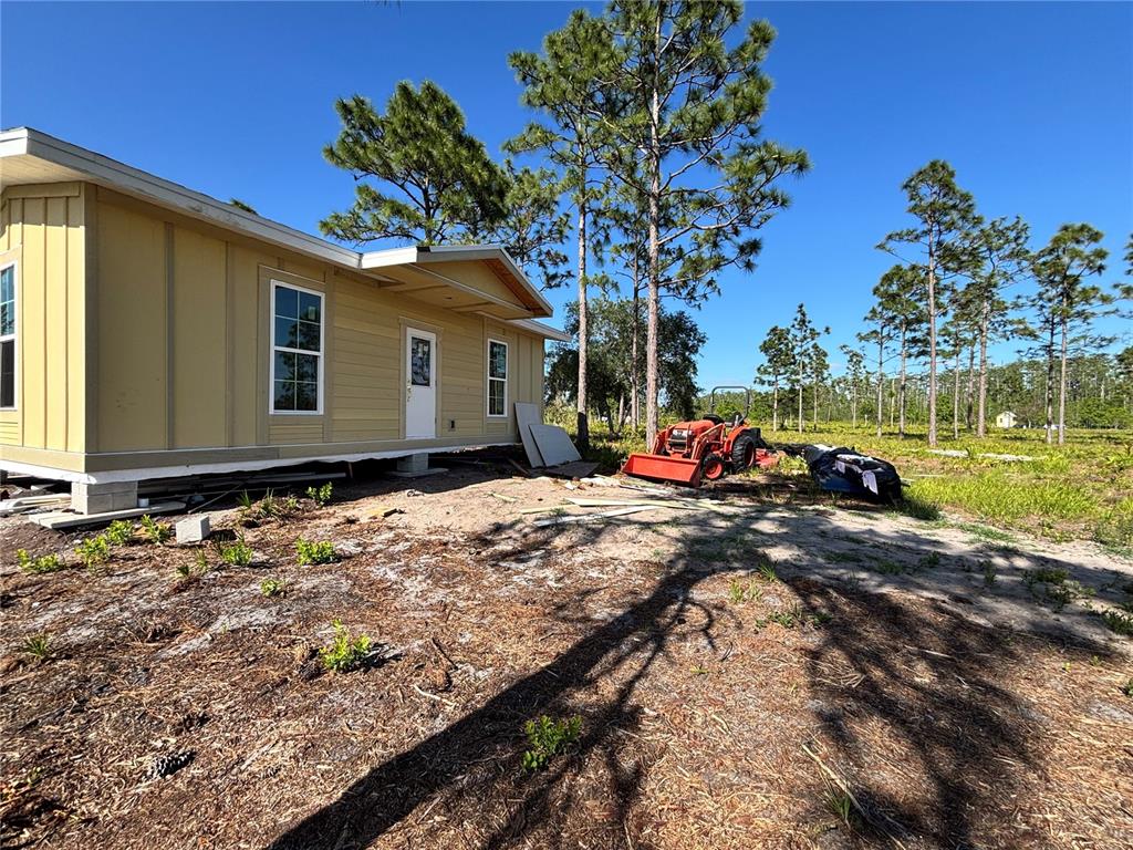 A tan manufactured home sits on a sandy lot with a tractor parked nearby — HARRIS ROAD, ST CLOUD, FL