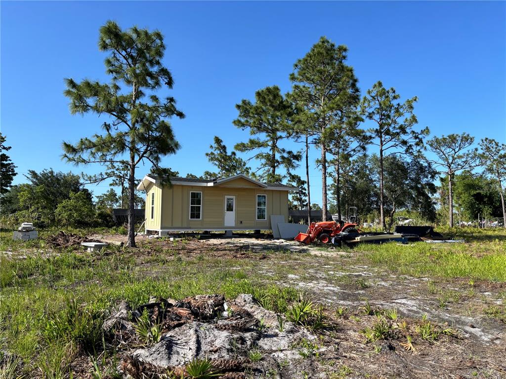 A yellow modular home sits on a grassy lot surrounded by pine trees — HARRIS ROAD, ST CLOUD, FL