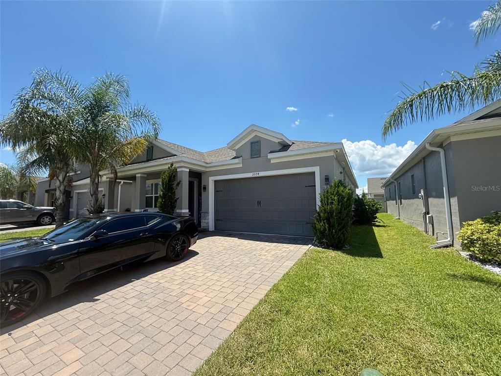 A single-story house with a gray garage, a paved driveway, and palm trees under blue sky — 2074 BRILLANTE DRIVE, ST CLOUD, FL