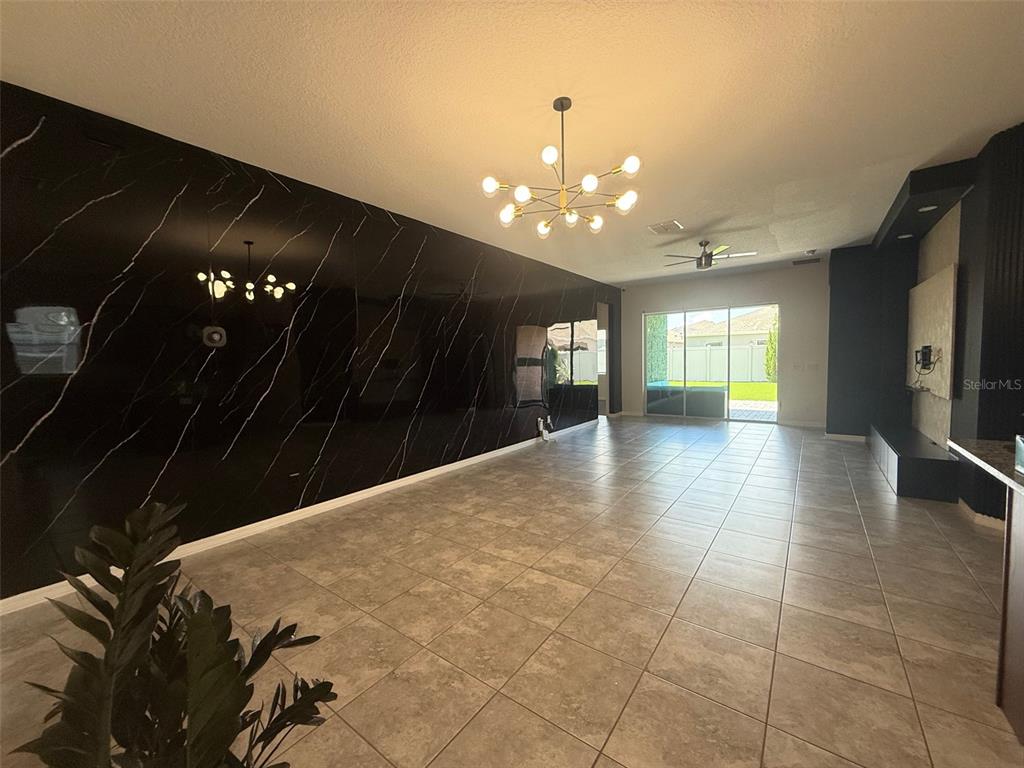 A living room features a large black marble accent wall, tile flooring, and a modern chandelier — 2074 BRILLANTE DRIVE, ST CLOUD, FL