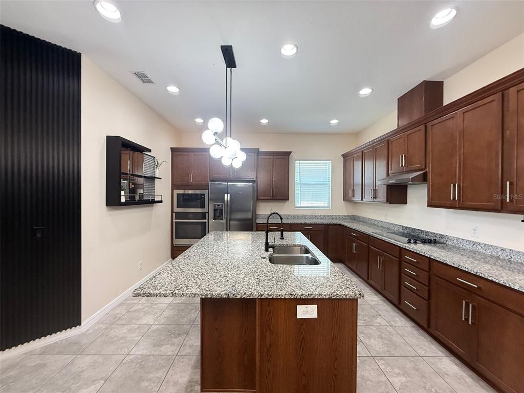 A kitchen features dark wood cabinets, granite countertops, a central island, and a modern light fixture — 2074 BRILLANTE DRIVE, ST CLOUD, FL