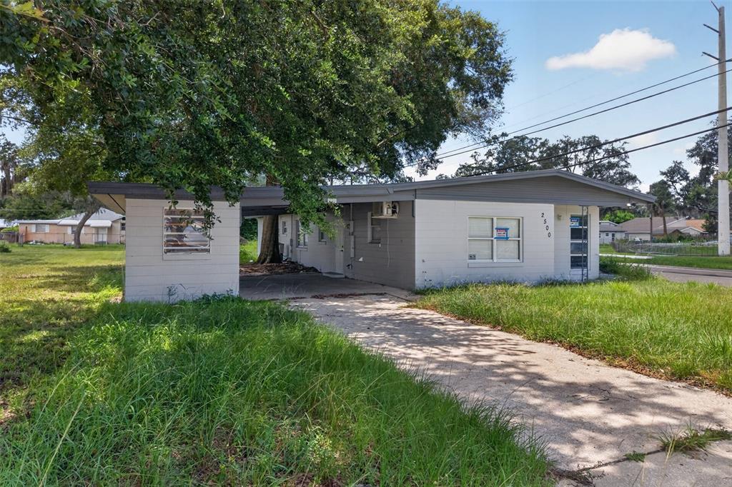 A single-story house with a white concrete block exterior, a carport, and an overgrown lawn — 2500 MYRTLE AVENUE, SANFORD, FL