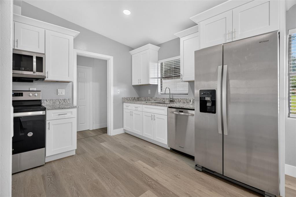 A kitchen with white cabinets, granite countertops, stainless steel appliances, and light wood-look flooring — 2500 MYRTLE AVENUE, SANFORD, FL