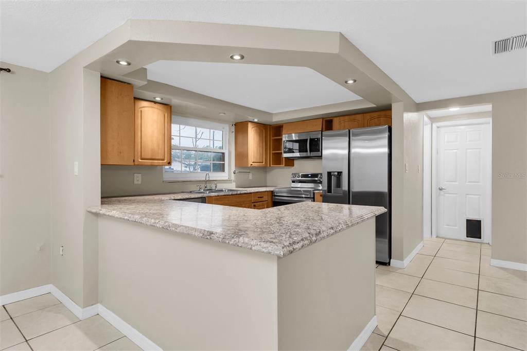A kitchen with light wood cabinets, granite countertops, stainless steel appliances, and tile flooring — 9203 GREENBRIAR LANE, PORT RICHEY, FL