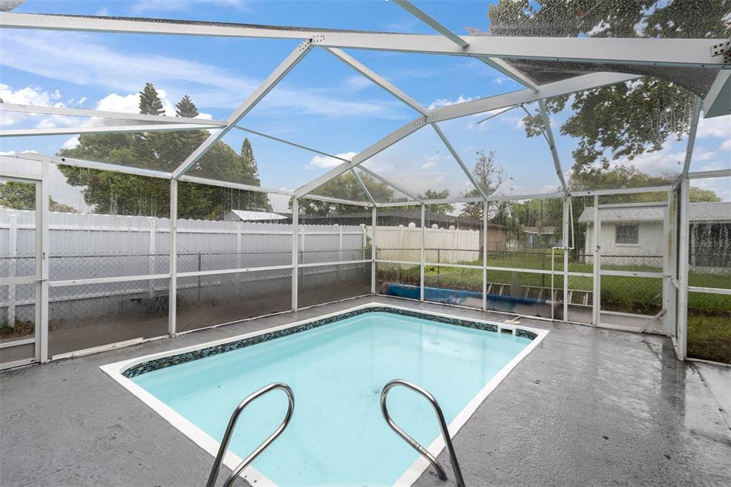 A rectangular swimming pool is enclosed by a white metal screen cage in a backyard — 9203 GREENBRIAR LANE, PORT RICHEY, FL