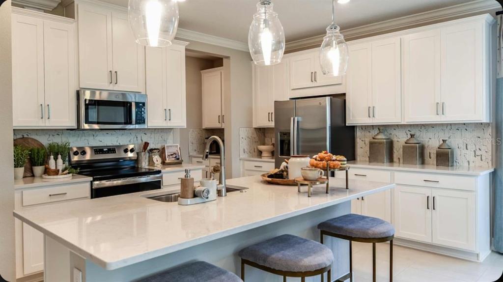 A modern kitchen features white cabinets, a large quartz island, and stainless steel appliances — 23 GEOSAM DRIVE, PALM COAST, FL