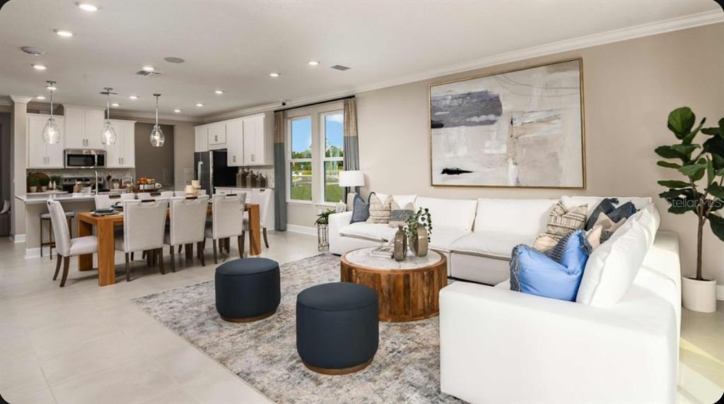 An open-concept living room and dining area featuring white furniture, a large rug, and kitchen — 23 GEOSAM DRIVE, PALM COAST, FL