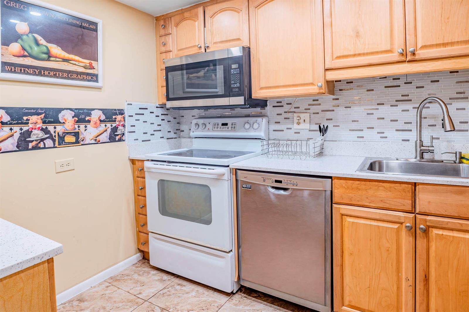 A kitchen features light wood cabinets, stainless steel appliances, a white stove, and tiled backsplash — 3710 Inverrary Drive # 2s, Lauderhill FL 33319, LAUDERHILL, FL
