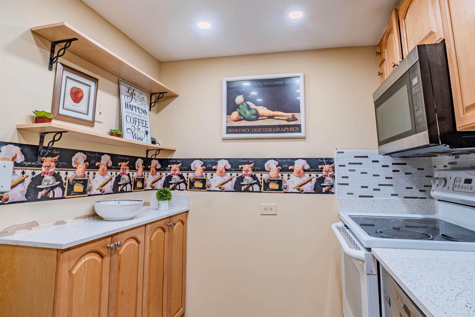 A kitchen features wood cabinets, a white countertop, a stove, and pig-themed wallpaper border — 3710 Inverrary Drive # 2s, Lauderhill FL 33319, LAUDERHILL, FL