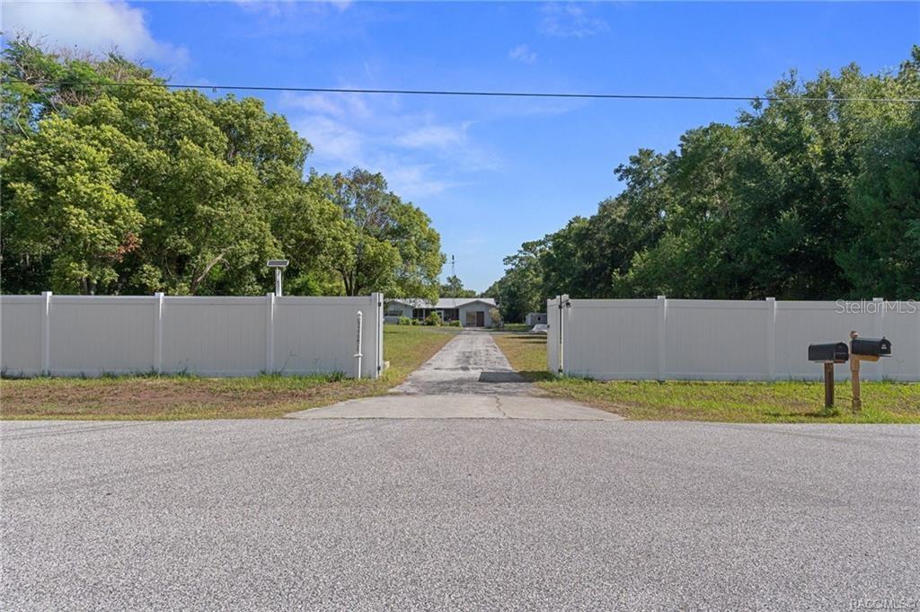 A concrete driveway leads through a white vinyl fence to a house surrounded by trees — 7251 W LACEY LANE, HOMOSASSA, FL