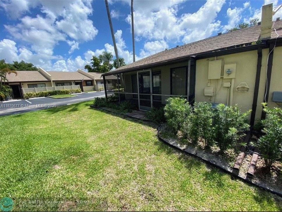 A view of a screened-in patio and landscaped yard next to a tan residential building — 715 Banks Rd, Margate FL 33063, MARGATE, FL