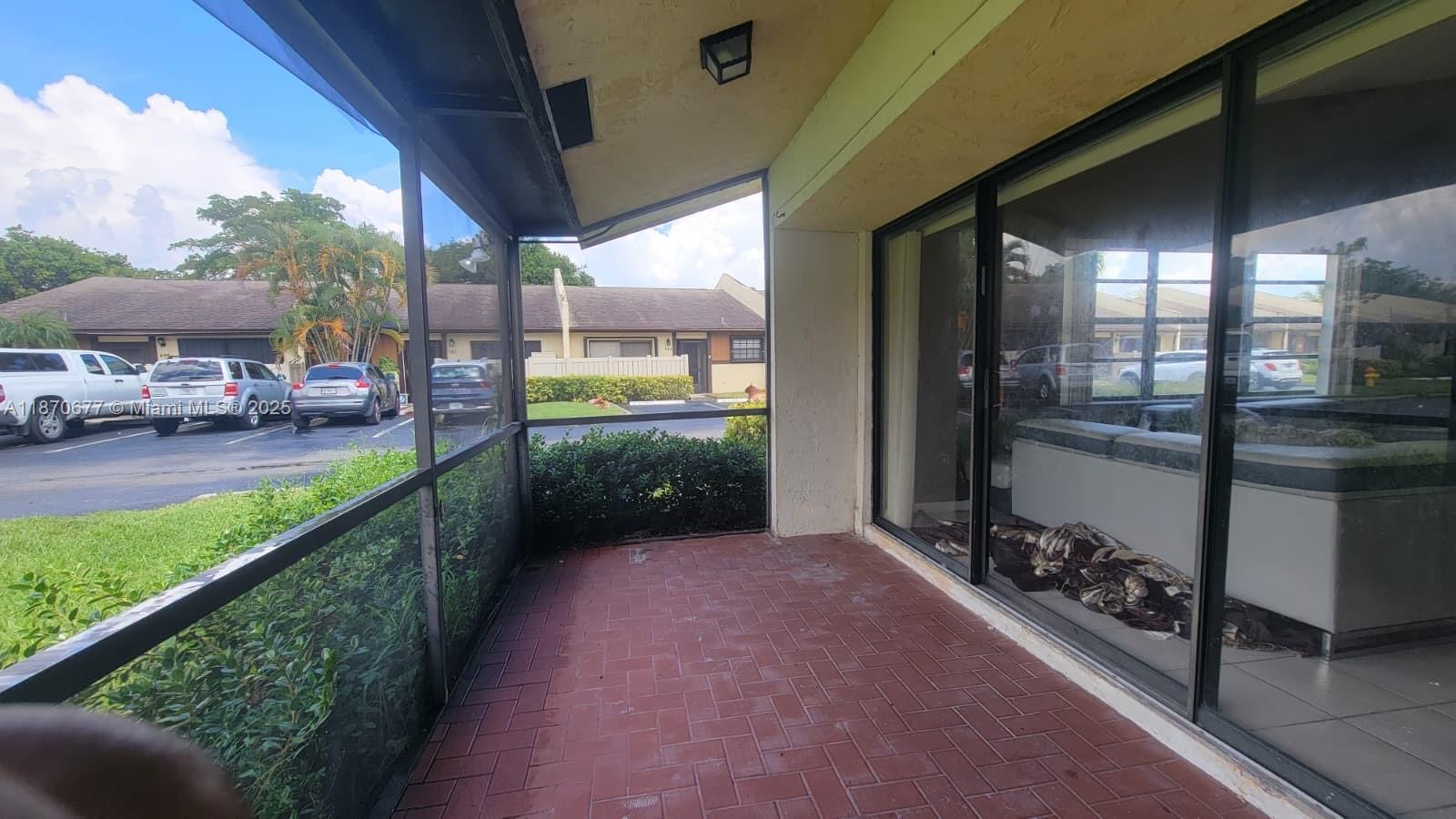 A screened-in patio with red brick pavers overlooks a parking lot and residential buildings — 715 Banks Rd, Margate FL 33063, MARGATE, FL