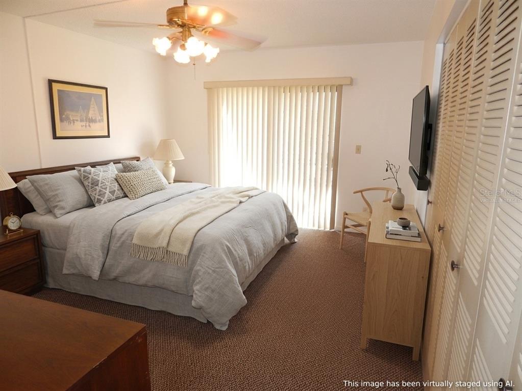 A bedroom with a bed, dresser, wall-mounted television, and sliding glass doors with vertical blinds — 215 LA CASA UNIT 215, LAKE WALES, FL