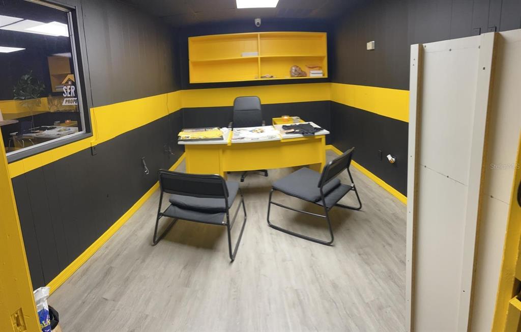 An office room features black and yellow walls, a yellow desk, and light wood flooring — 1210-1232 DYER BOULEVARD UNIT 1214, KISSIMMEE, FL