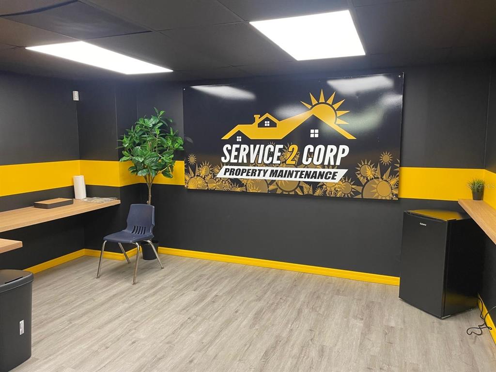An office space features gray wood-look flooring, black walls with yellow trim, and a company sign — 1210-1232 DYER BOULEVARD UNIT 1214, KISSIMMEE, FL