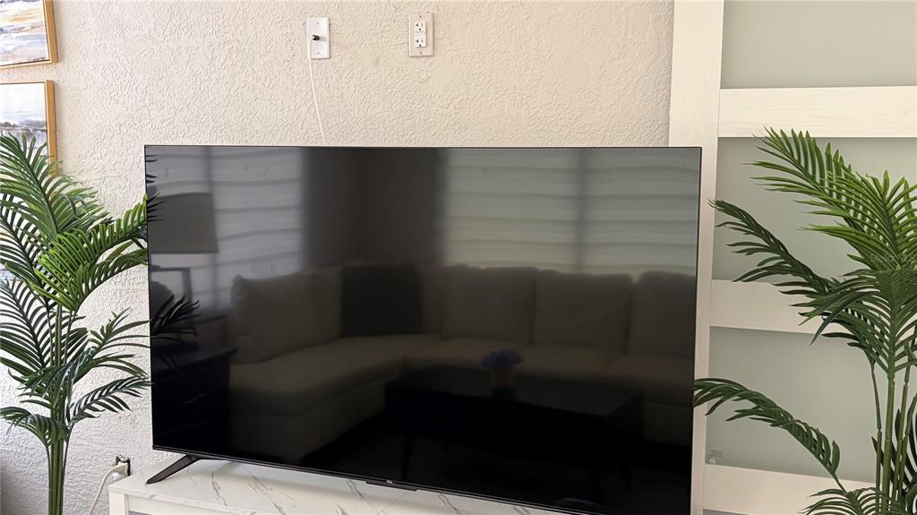 A large television sits on a white marble-patterned console between two potted artificial palm trees — 389 NOLANE LANE, POLK CITY, FL