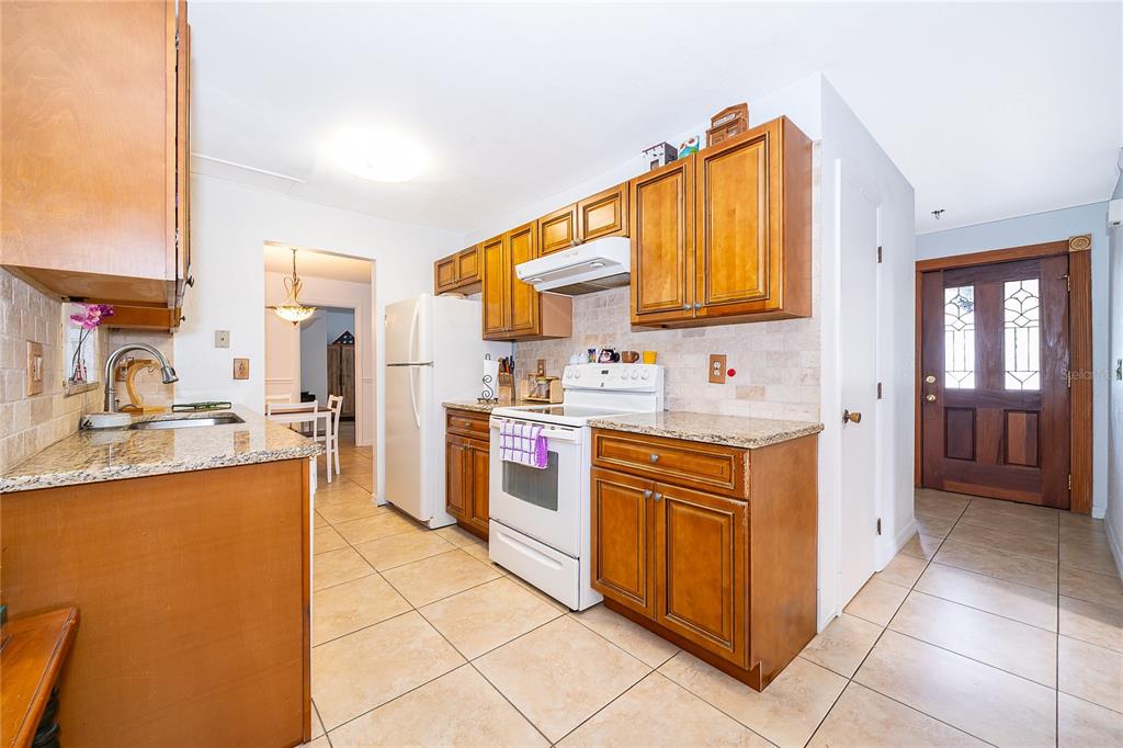 A kitchen with wood cabinets, granite countertops, tile flooring, and a white stove — 103 KILKENNY COURT, LONGWOOD, FL